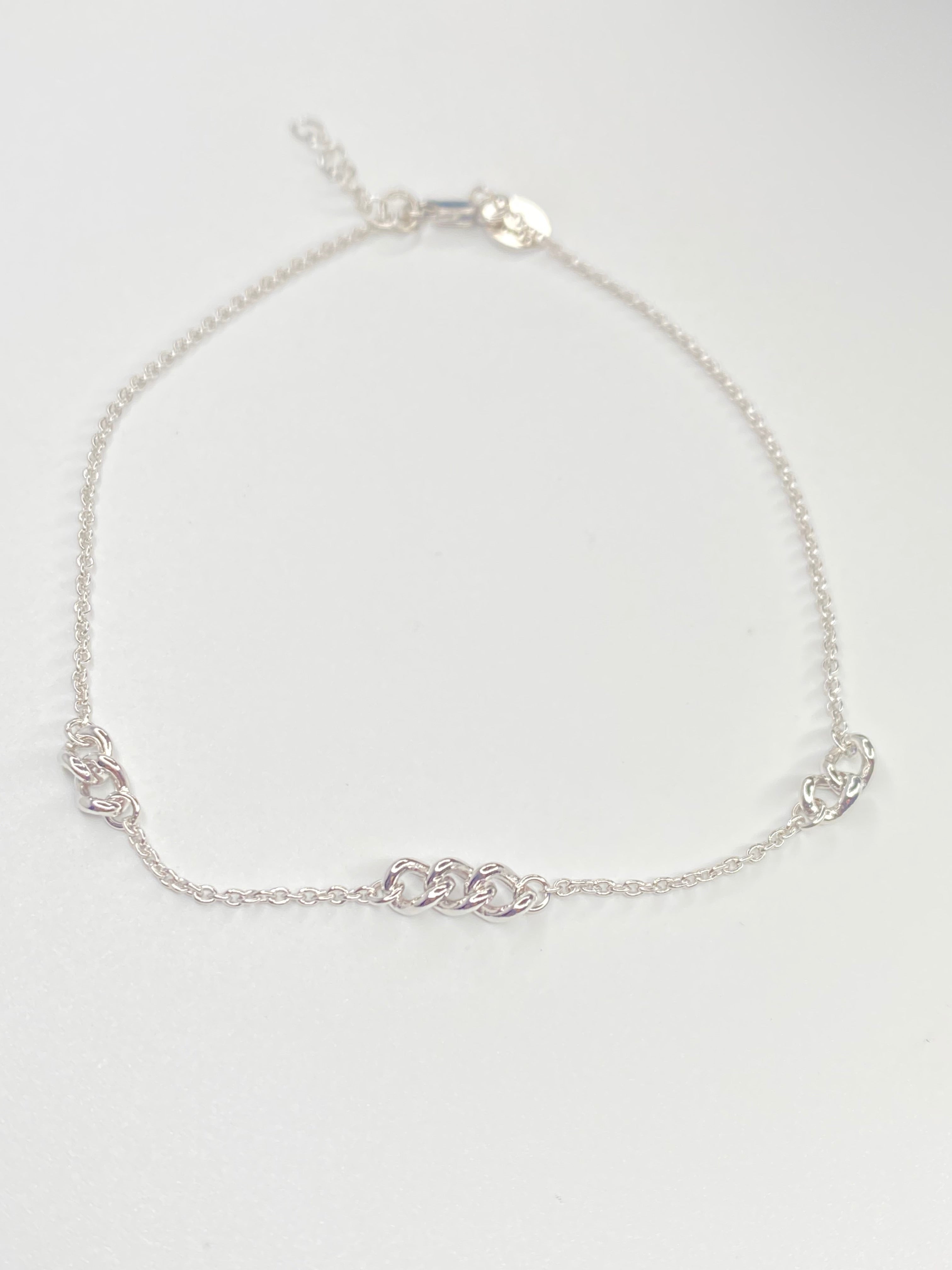 A delicate silver chain anklet with a alternative thicket link design with the cable link displayed on a clean white background.