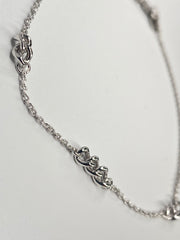 A silver chain anklet featuring three interlocking  link designs spaced along the chain, photographed on a plain light background.