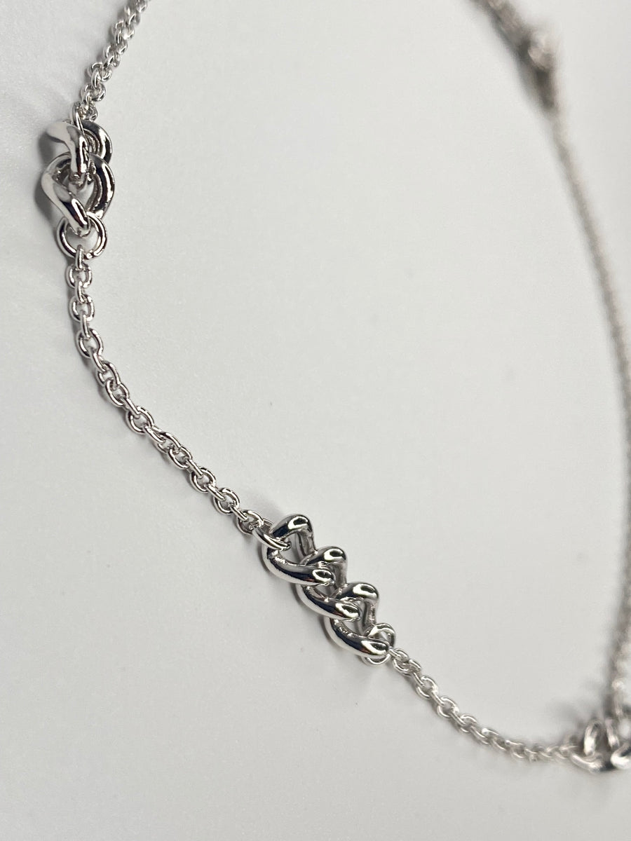 A silver chain anklet featuring three interlocking  link designs spaced along the chain, photographed on a plain light background.