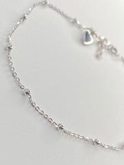 A delicate sterling silver chain anklet with small bead accents and a small heart charm, displayed on a light gray background.