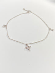 A delicate silver chain ankelt featuring a small cross charm set with clear stones, displayed on a clean white background.