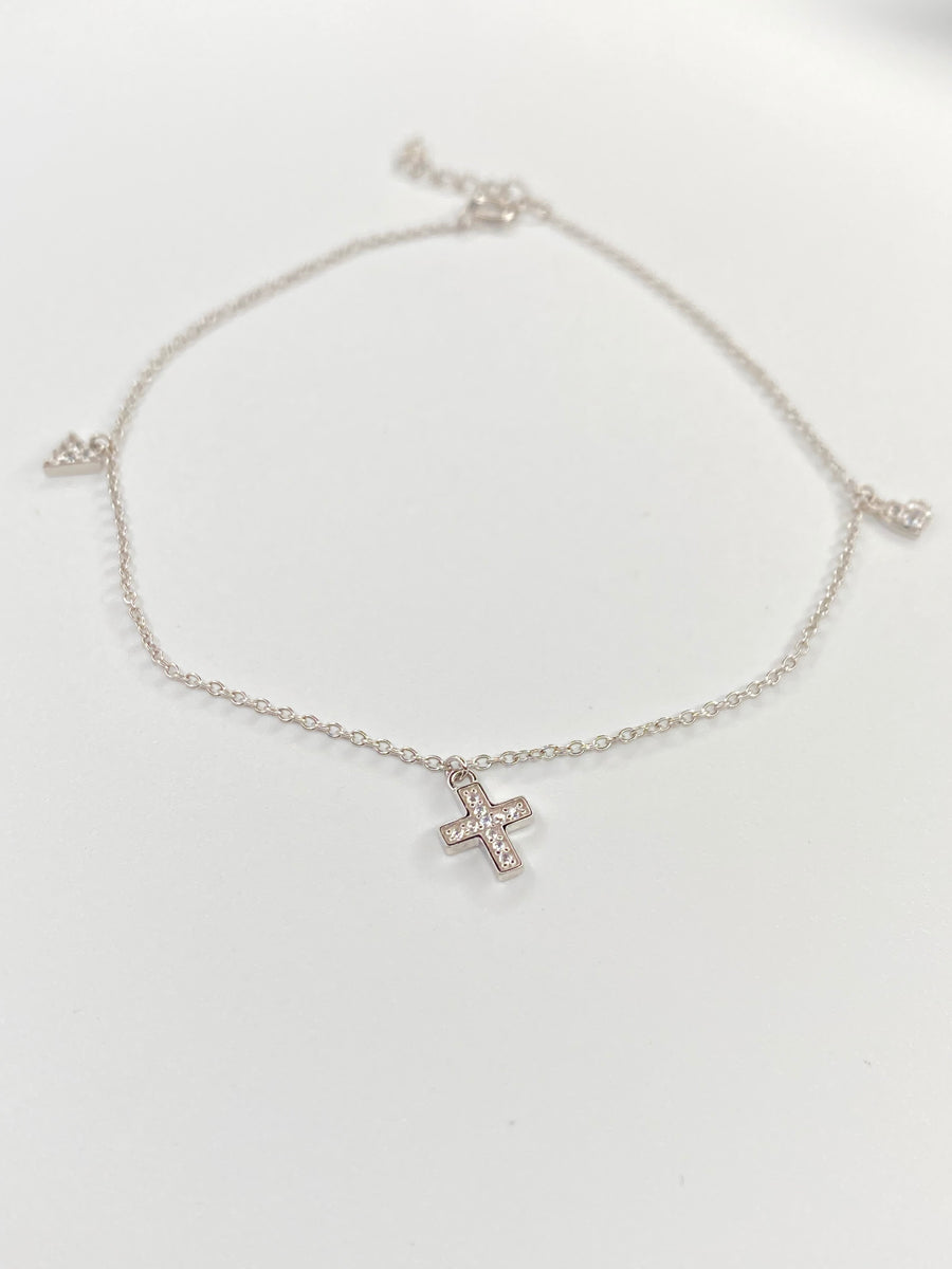 A delicate silver chain ankelt featuring a small cross charm set with clear stones, displayed on a clean white background.