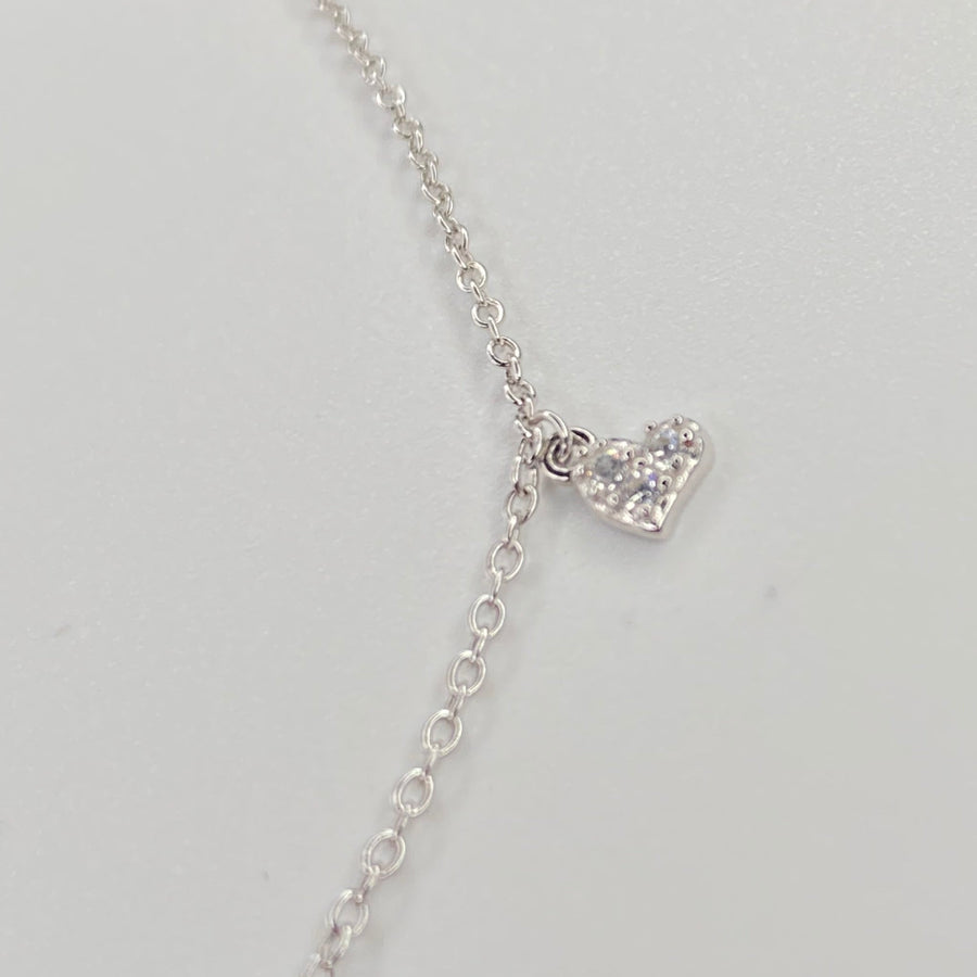 A delicate silver chain anklet with a small pavé-set heart pendant, shown on a plain light gray background.