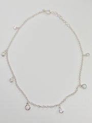 A delicate silver chain anklet with small dangling charms, displayed on a light gray background.