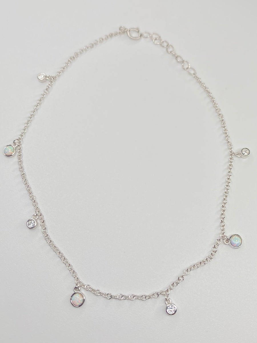 A delicate silver chain anklet with small dangling charms, displayed on a light gray background.