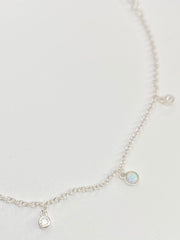 A delicate silver chain anklet with small dangling charms, including a opal like stones and clear cz round stones, displayed on a clean white background.